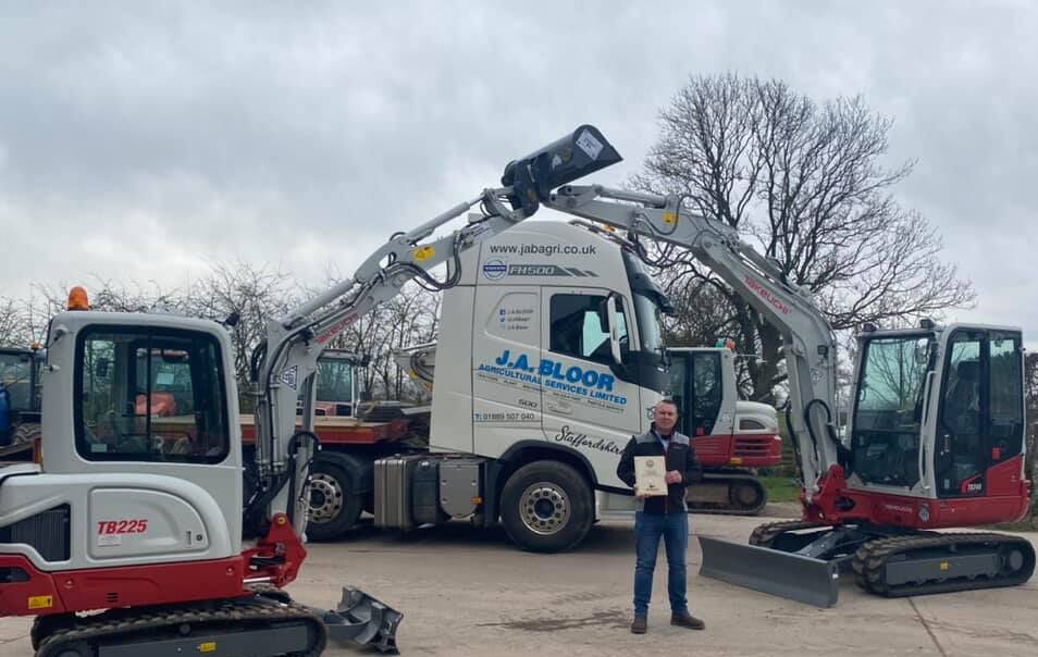 salesman standing in front of a wagon and two takeuchi diggers with their booms up in the air